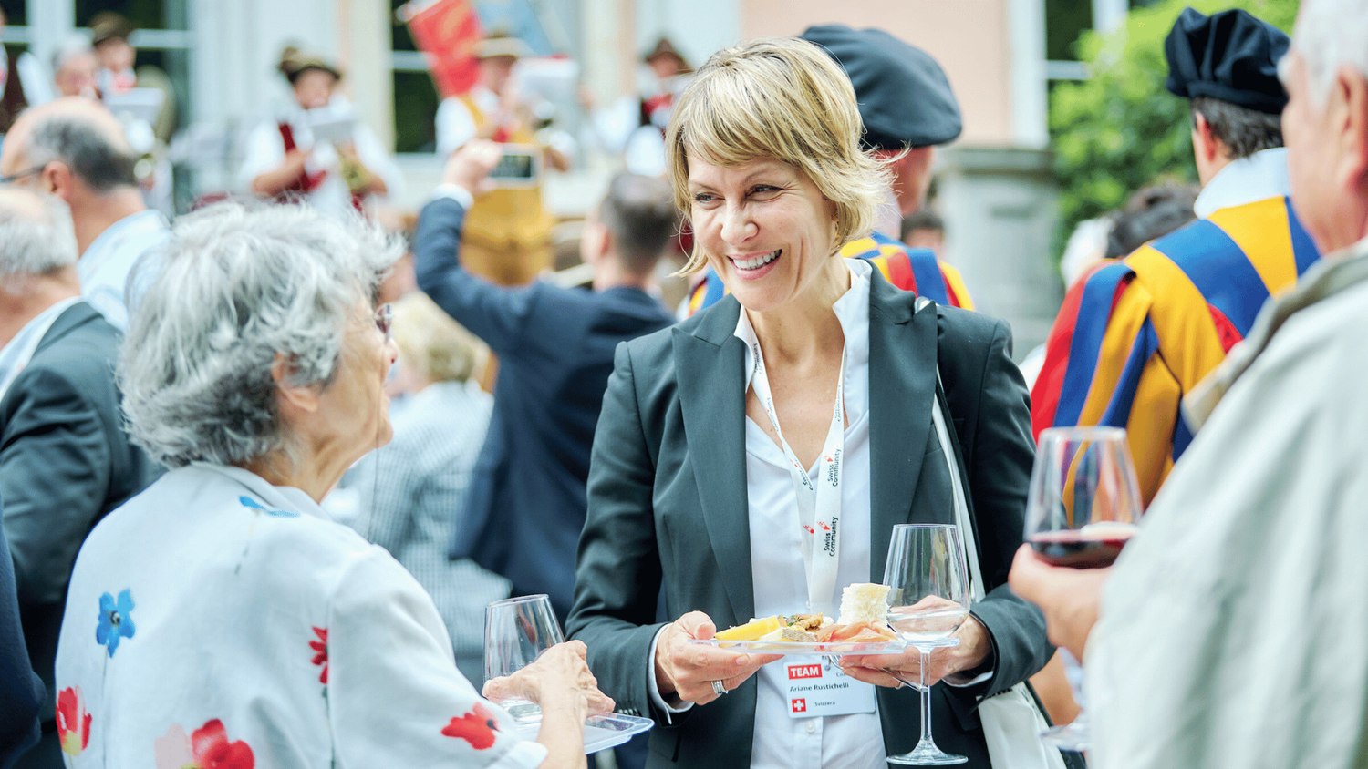 Apéritif debout dans un jardin. Ariane Rustichelli se tien au milieu des personnes.