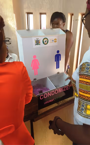 Des femmes africaines discutent autour d’une boîte à distribuer des moyens de contraceptions masculins et féminins.