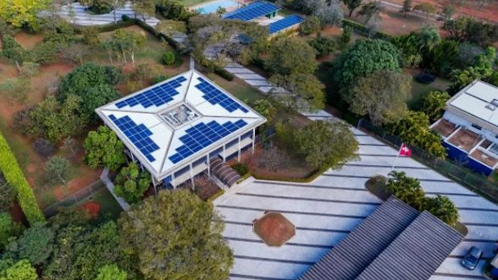 Prise de vue aérienne du site de l’ambassade à Brasília. La photo montre les différents bâtiments équipés de panneaux solaires ainsi que le vaste jardin de l’ambassade.