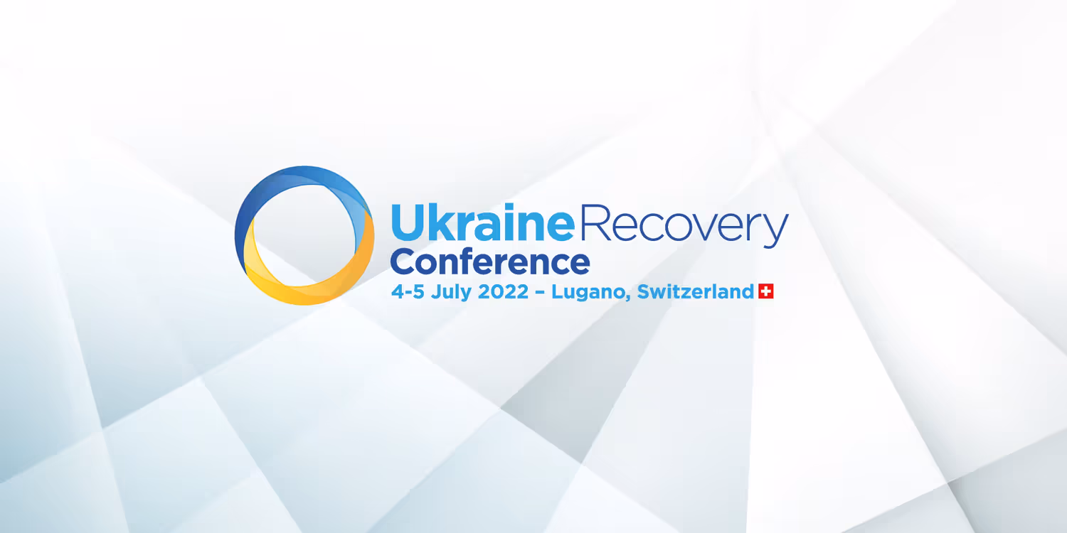 Le logo de l’Ukraine Recovery Conference 2022 comporte un cercle moitié jaune moitié bleu à côté duquel figurent des indications de lieu et de date (en bleu).