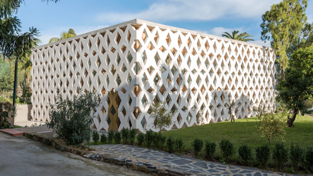 L’Ambasciata di Svizzera ad Algeri vista dall’esterno. L’edificio, di un bianco splendente, ha la forma di un parallelepipedo rettangolare. La facciata è costituita da numerose travi che si incrociano tra loro formando una sorta di grande griglia. 