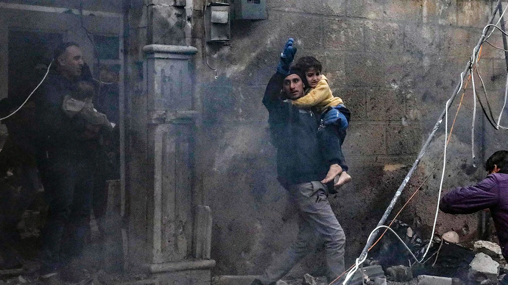 Un uomo tiene in braccio un bambino tra le macerie in Siria.