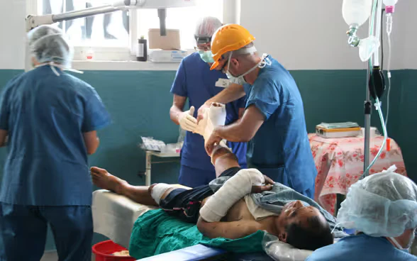 Tre medici in camice blu assistono un paziente nepalese che si è rotto un braccio e una gamba.