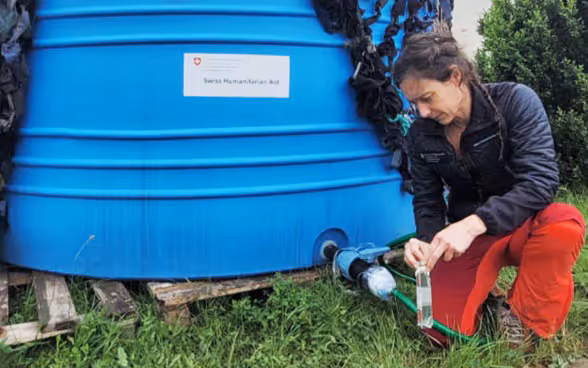 Una donna si inginocchia accanto a un serbatoio d'acqua e lascia scorrere l'acqua in una bottiglia.