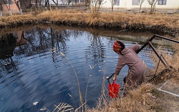 Una ragazza con una sciarpa rossa attinge acqua con un secchio.