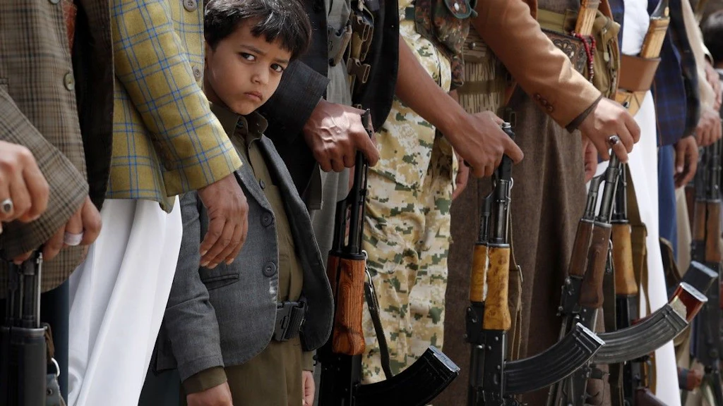Un bambino yemenita tra adulti armati.