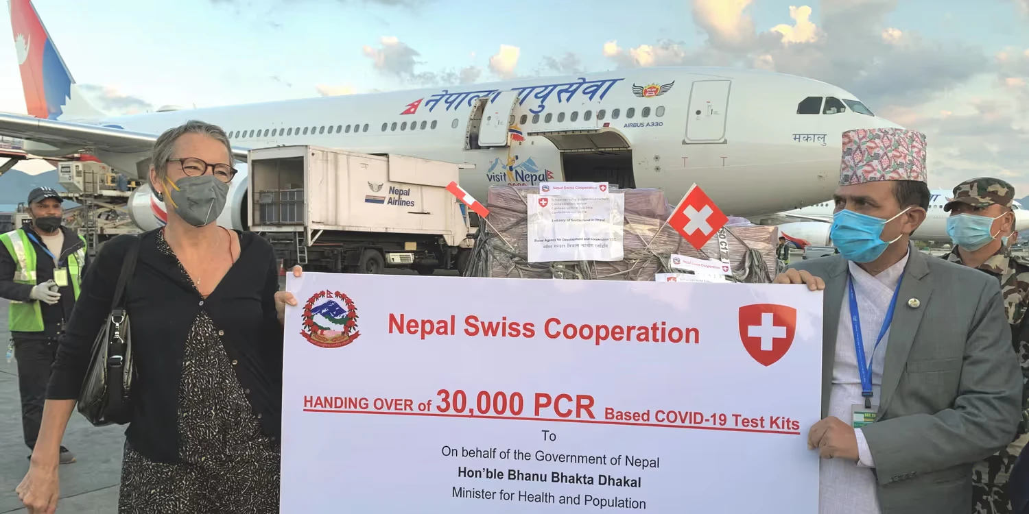 L’ambasciatrice svizzera in Nepal e il ministro nepalese della salute e della popolazione sono davanti a un aereo e tengono in mano un manifesto in cui è indicata la consegna di 30 000 kit diagnostici per il COVID-19.