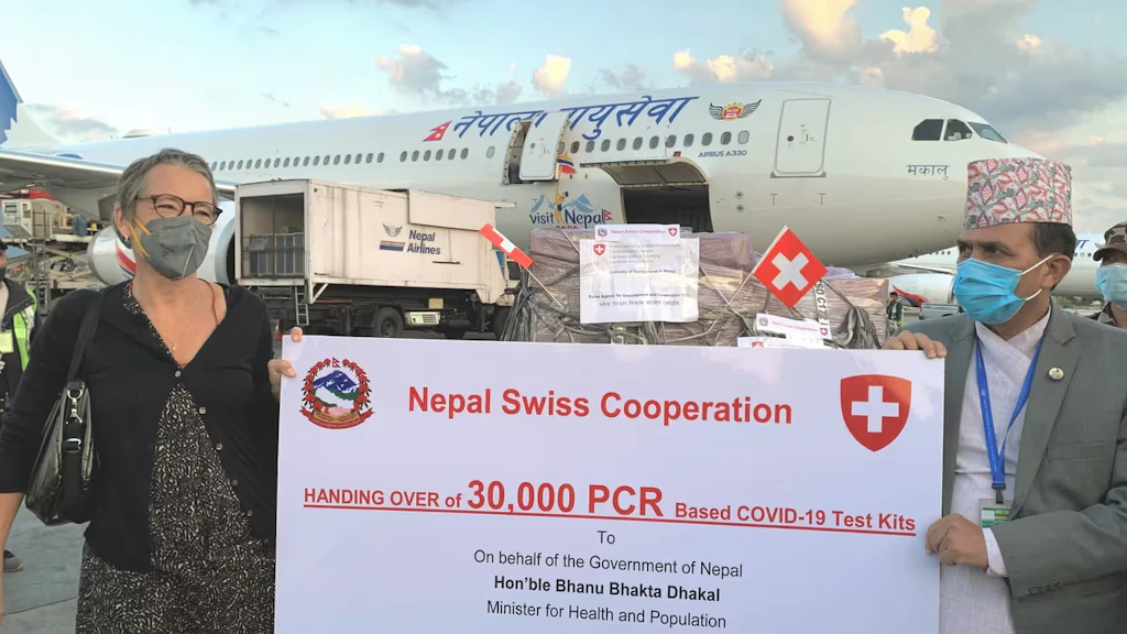 L’ambasciatrice svizzera in Nepal e il ministro nepalese della salute e della popolazione sono davanti a un aereo e tengono in mano un manifesto in cui è indicata la consegna di 30 000 kit diagnostici per il COVID-19.