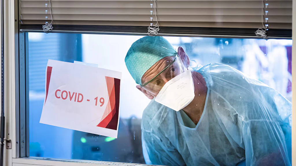 Dal reparto di terapia intensiva, un membro del personale infermieristico guarda attraverso una finestra su cui è apposta la scritta “Covid-19”.