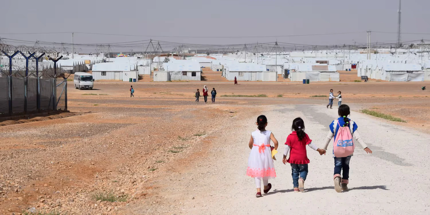 Tre ragazze camminano su un sentiero di ghiaia nel campo profughi di Azraq, nel mezzo del deserto giordano.