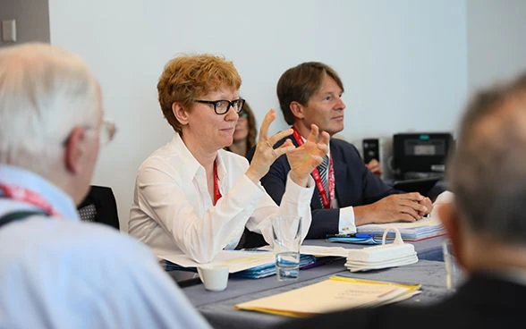 Kathrin Meyer, segretaria permanente dell’IHRA, a una seduta in occasione dell’assemblea plenaria dell’IHRA. Sullo sfondo il presidente in carica dell’IHRA Benno Bättig.