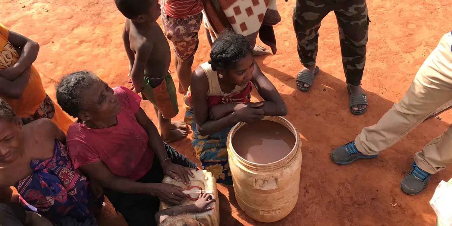 L'immagine mostra donne, bambini e un uomo armato riuniti intorno a un bollitore di acqua sporca.