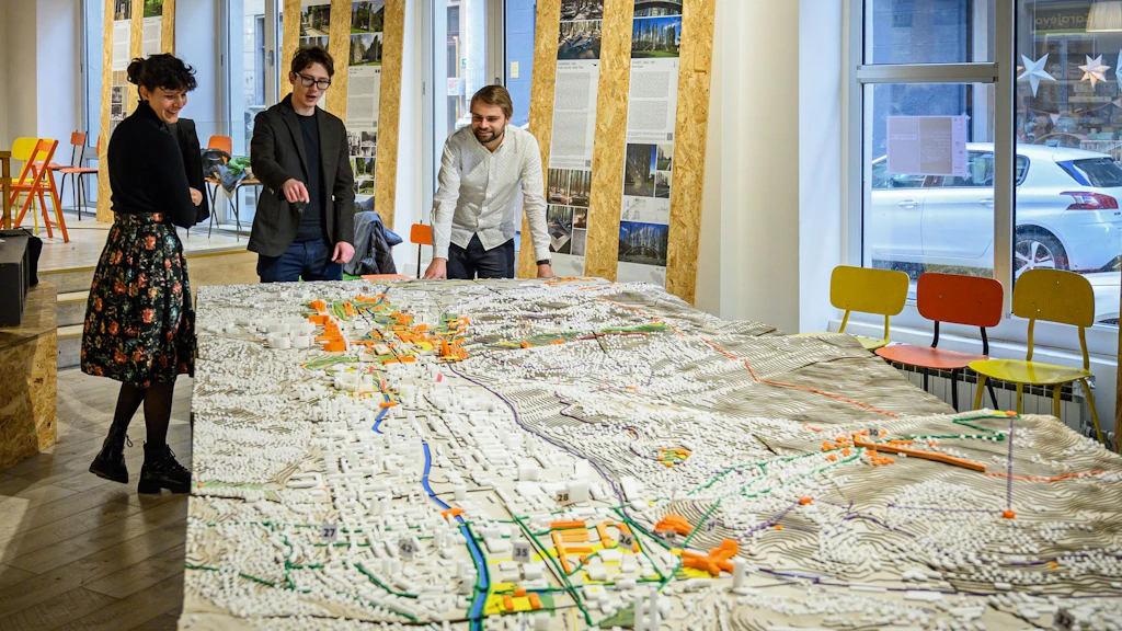 Tre persone discutono in una stanza davanti a un grande plastico della città di Sarajevo.