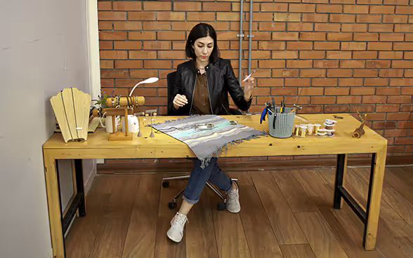 Una giovane imprenditrice irachena seduta a un tavolo di legno realizza gioielli.