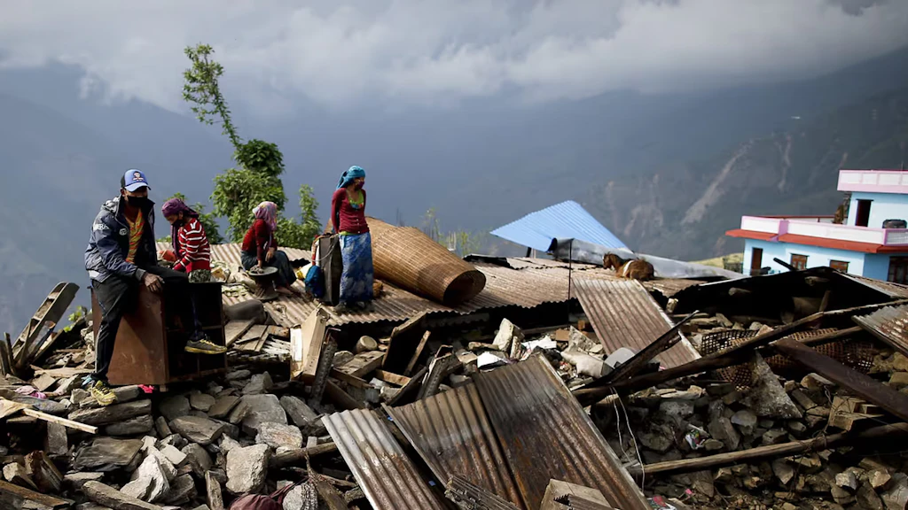 Una famiglia nepalese con due bambini siede sulle macerie della propria casa in un villaggio di montagna.