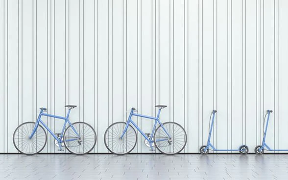 Biciclette e monopattini appoggiati a un muro. 