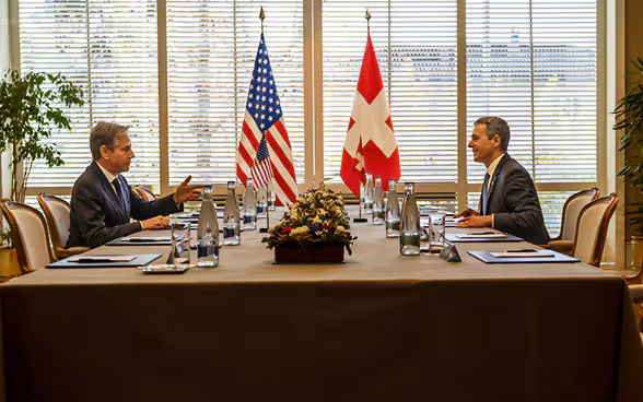 Ignazio Cassis e il ministro degli esteri Blinken siedono uno di fronte all'altro a un tavolo e parlano.