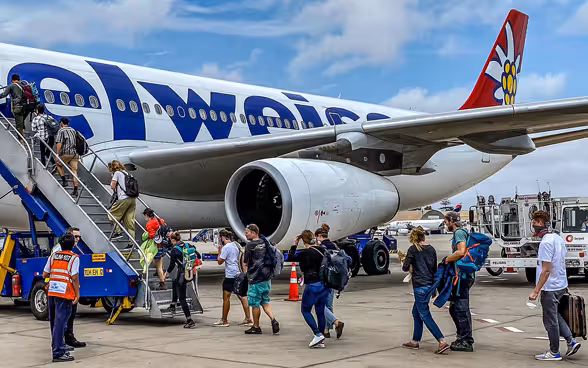Un aereo, con le scale d’accesso, sui cui salgono alcuni passeggeri per imbarcarsi.
