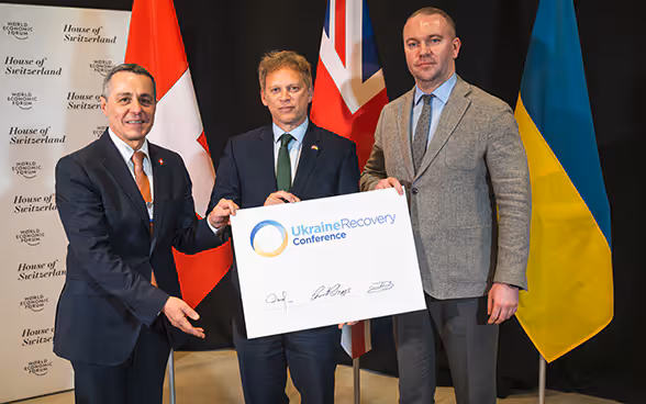 Il consigliere federale Cassis, il ministro britannico Grant Shapps e il segretario di Stato del ministero degli affari esteri ucraino Oleksandr Bankov, si trovano uno accanto all'altro e tengono insieme un documento.