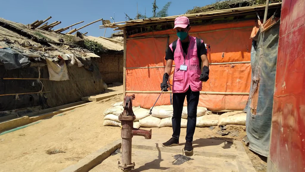 Un uomo con una giacca rosa disinfetta un pozzo in un campo profughi in Bangladesh. 