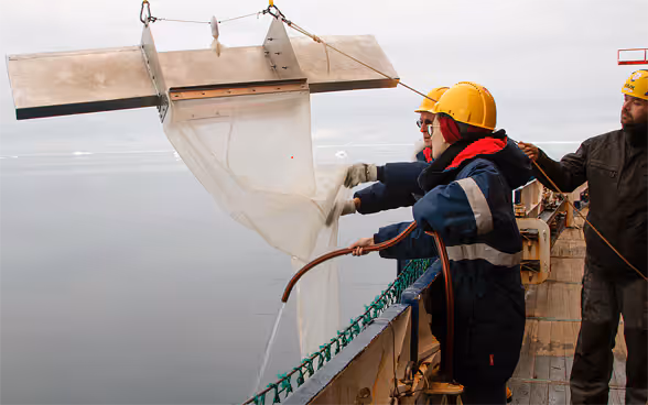 Tre scienziati maneggiano attrezzature su una barca e indossano caschi gialli in testa.