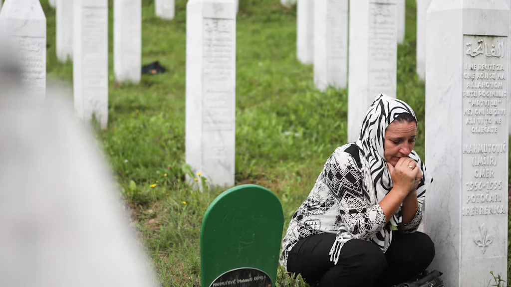 Una donna si inginocchia accanto a una lapide nel cimitero di Srebrenica.
