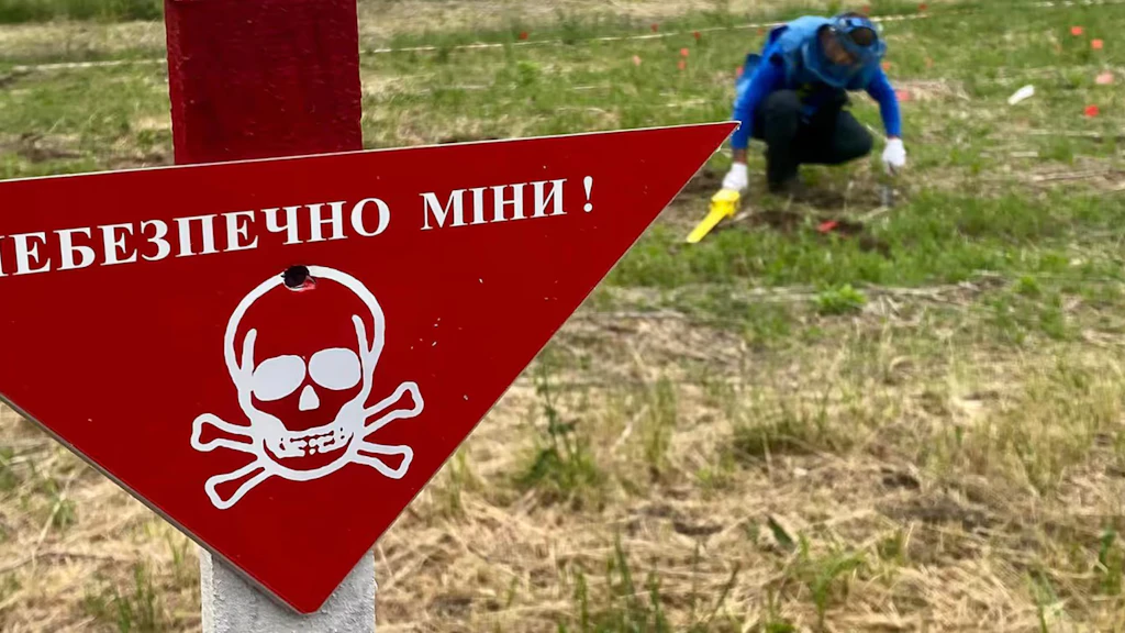 Un uomo in abbigliamento protettivo lavora in un campo con un cartello di pericolo di morte.
