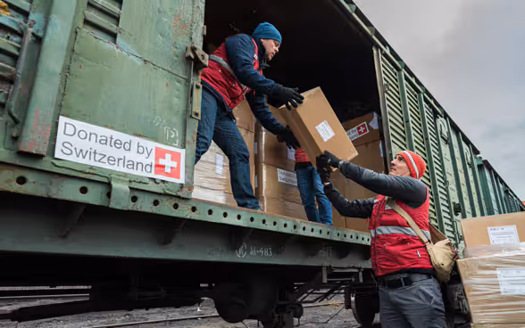 Del materiale diretto in Ucraina viene caricato da due persone su un vagone del treno che riporta la scritta "Donated by Switzerland".  