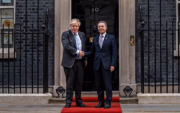 Il consigliere federale Ignazio Cassis e il primo ministro Boris Johnson in piedi su un tappeto rosso davanti all'ingresso della residenza del primo ministro al numero 10 di Downing Street. Si stringono la mano.