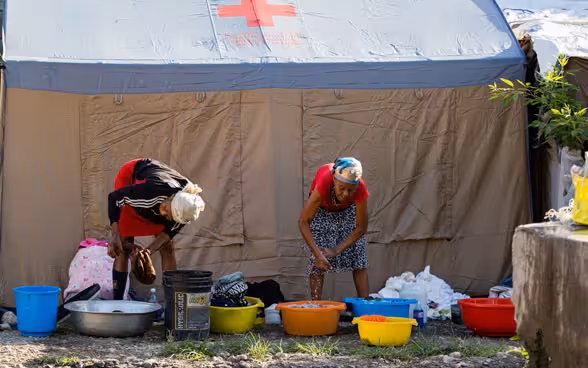 Donne di Haiti lavano il bucato in vasche di plastica davanti a una tenda con una croce rossa.